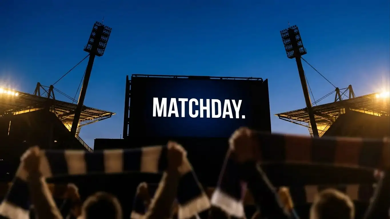 A close-up of a stadium big-screen style scoreboard silhouette against a clear evening sky, supporters' scarves raised in the foreground